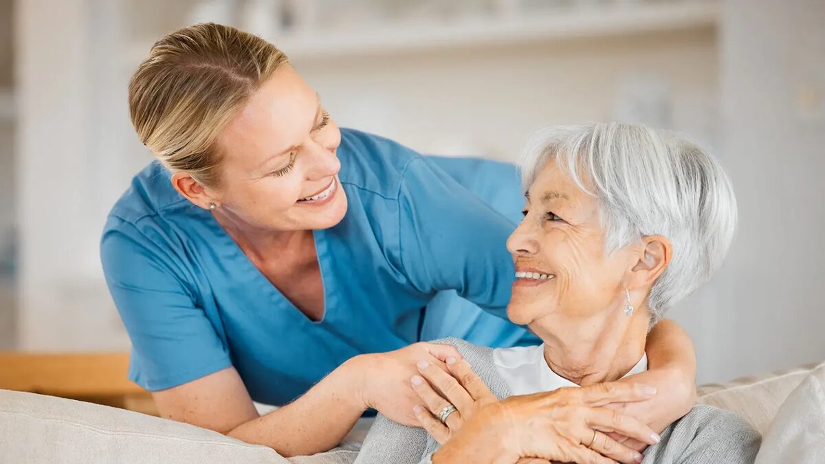 Cuidadora sonriendo junto a una residente adulta mayor en una ELEAM